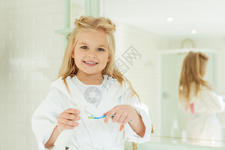 穿着浴袍的可爱小女孩拿着牙刷和牙膏在图片