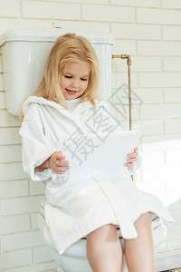 穿着浴袍的可爱笑着微笑的小女孩在坐厕所时使用图片