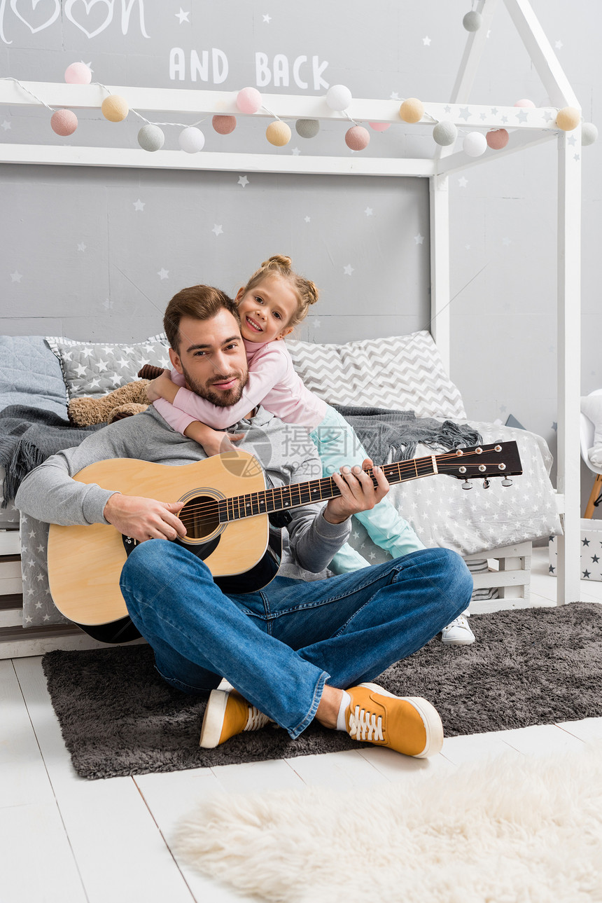 父亲在孩子卧室的地板上为女儿弹吉他图片