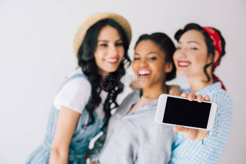 多元文化幸福妇女选择地关注在智能手机上自拍的孤立于灰色地带的多图片