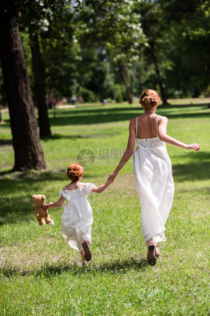 母亲和女儿背面看到泰迪熊手牵同时在公园图片