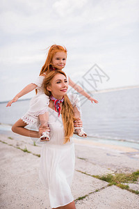 快乐的年轻母亲带着可爱的小女儿在海边走图片