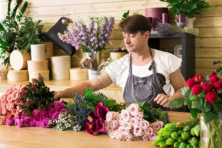 小本生意男花店在花店制作玫瑰花束花艺设计工作室的男助理或老板图片