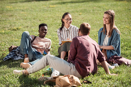 多种族青年学生群体在坐草地上学习和微笑时相图片