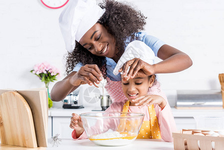 快乐的非洲母亲和女儿在厨师帽子上做图片
