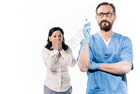 害怕的女病人用注射器看医生被白色隔离图片