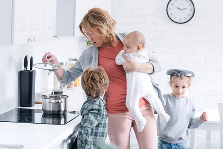 在厨房玩耍的淘气儿童时抱着婴儿和做饭的图片