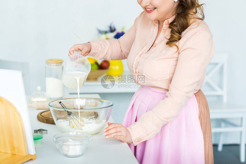 厨房用面粉将牛奶倒进碗中的妇图片