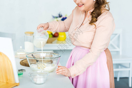厨房用面粉将牛奶倒进碗中的妇图片