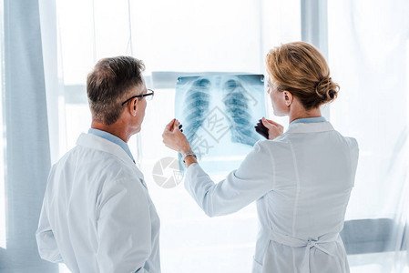 戴眼镜的医生看着同事手中的X光片图片