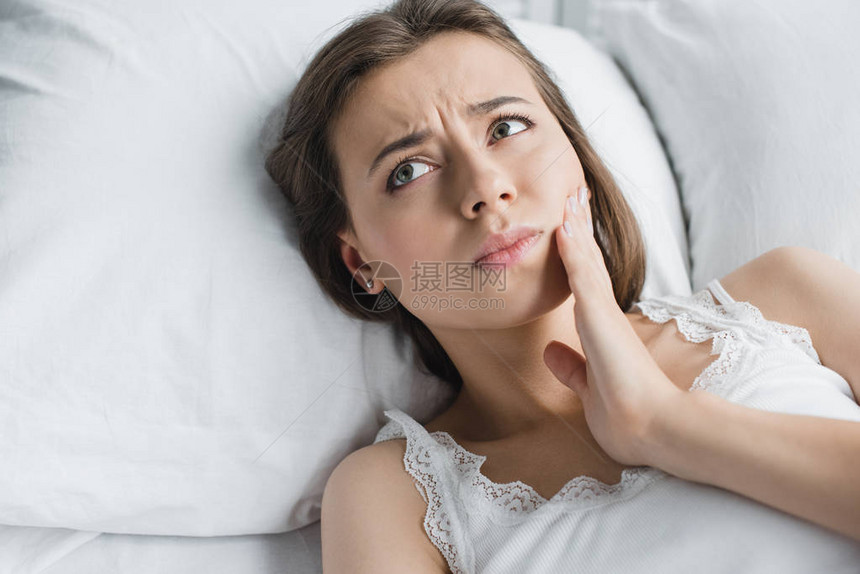 有吸引力的年轻女子因牙痛和躺在床上时视图片