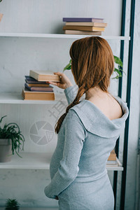 孕妇从家里书架上拿书的侧面图图片