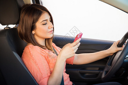 一位鲁莽的拉丁美洲年轻女驾驶汽车时使用智能图片