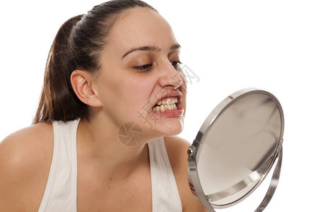 年轻女子在镜子里检查她的牙齿图片
