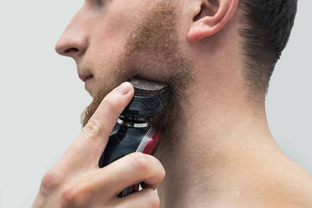 年轻时髦男子用电动剃须刀机剃姜胡须剃须的侧面图图片