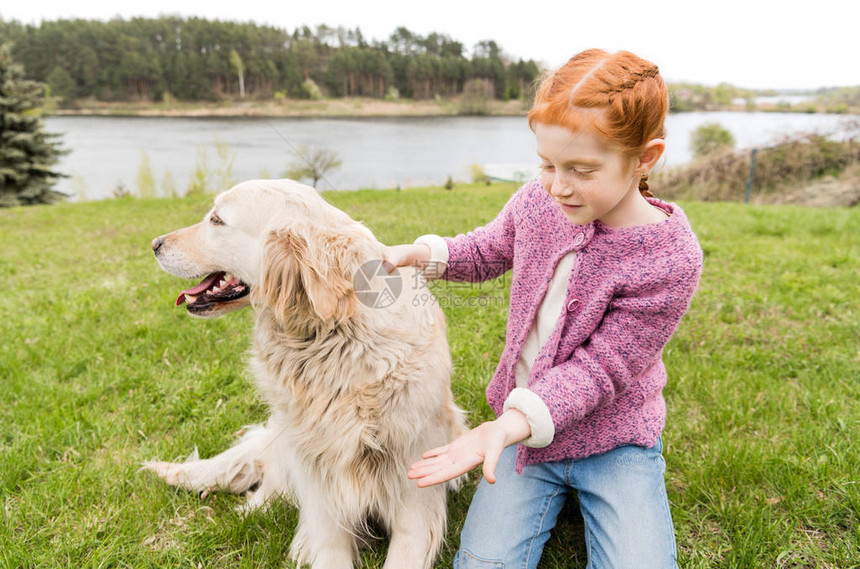 可爱的红发女孩跪在绿草地上和狗玩耍图片