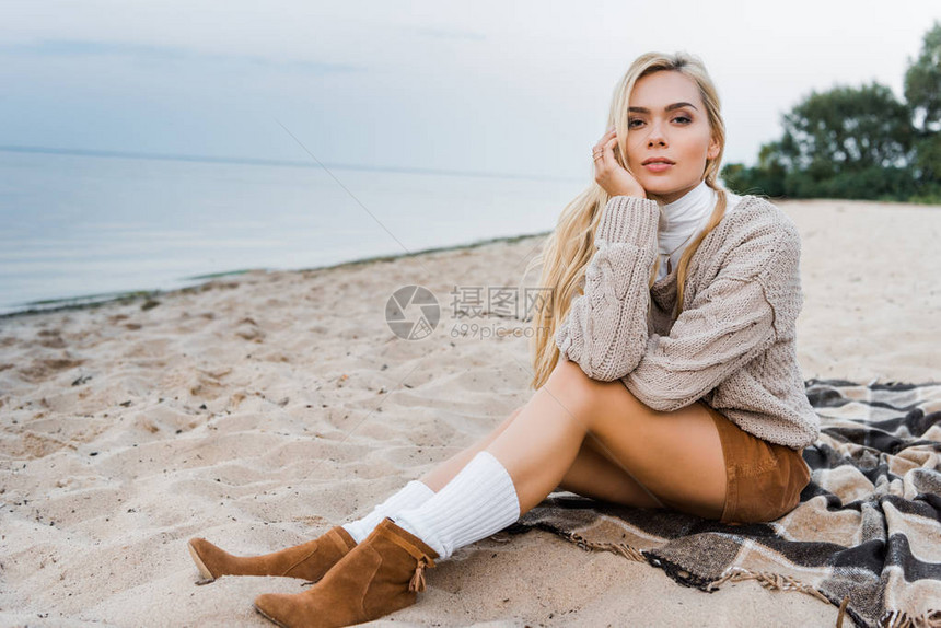 穿着秋装的漂亮金发美女坐在海滩上手靠着下巴图片
