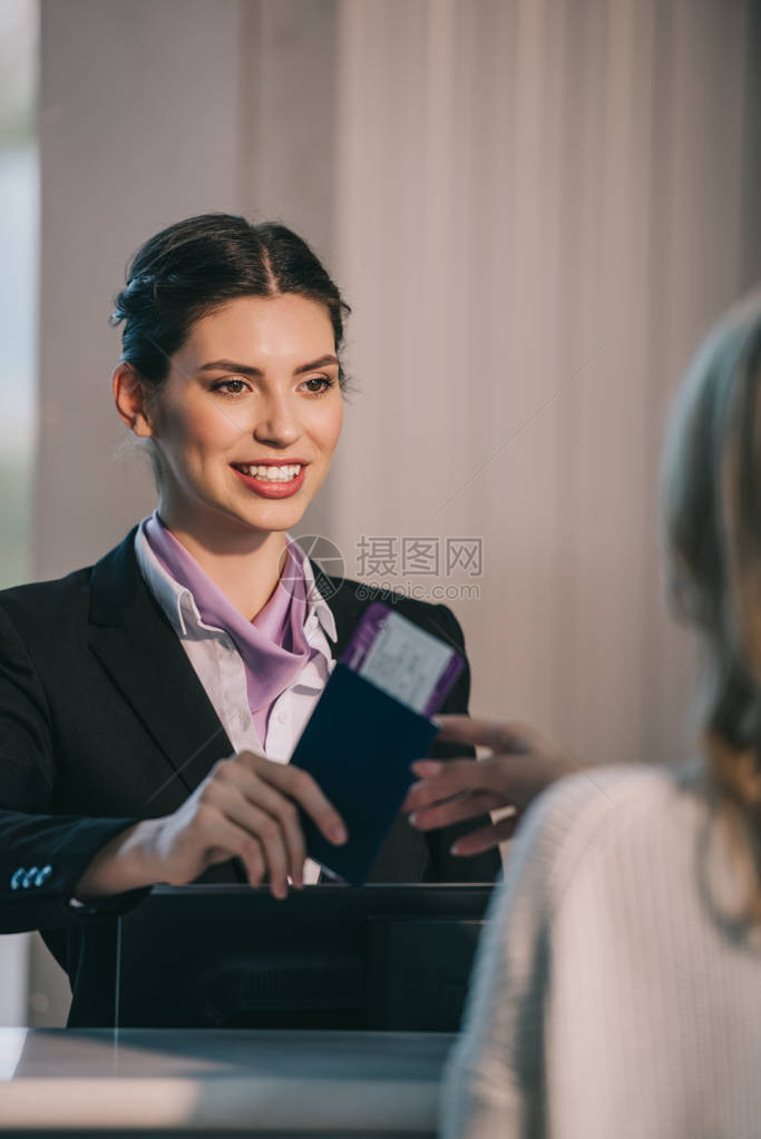 在机场报到台向年轻旅行者发放带登机证的护照时微笑着微笑的工图片