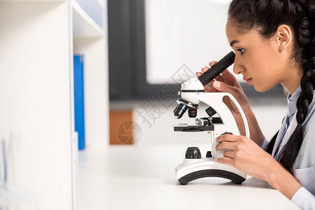 在实验室与显微镜合作的实验室外衣中年轻科学图片
