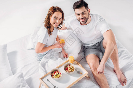 以木质托盘为早餐的年轻夫妇在床上看镜头图片