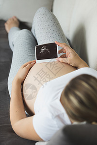 年轻孕妇在沙发上躺着看超声波婴图片
