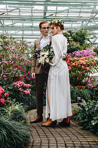 在植物园的花朵之间站在一起看着整个美丽的年轻优雅婚礼情图片