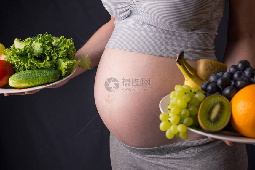 一个有肚子的孕妇手里拿着一盘水果和蔬菜孕期体重控制和健图片