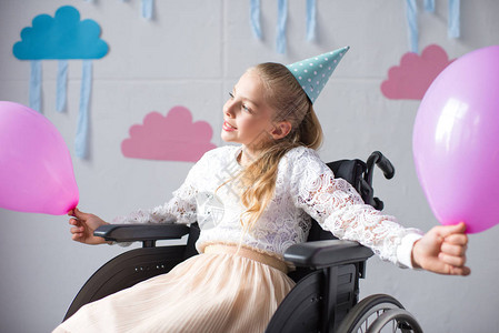戴着生日帽的美丽微笑女孩坐在轮椅上图片