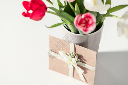 花瓶中美丽盛开的郁金香花和灰色信封的选择焦点图片