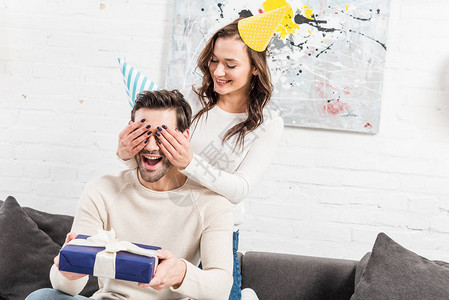女人在派对的帽子闭上眼睛和做生日惊喜与礼物给男人图片