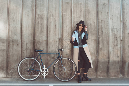 穿秋装的时髦女人和黑色太阳眼镜站在自行车旁边握着奶昔看图片