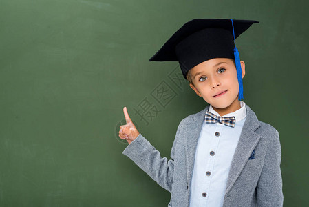 穿着毕业帽子的中学生指着黑板旁图片