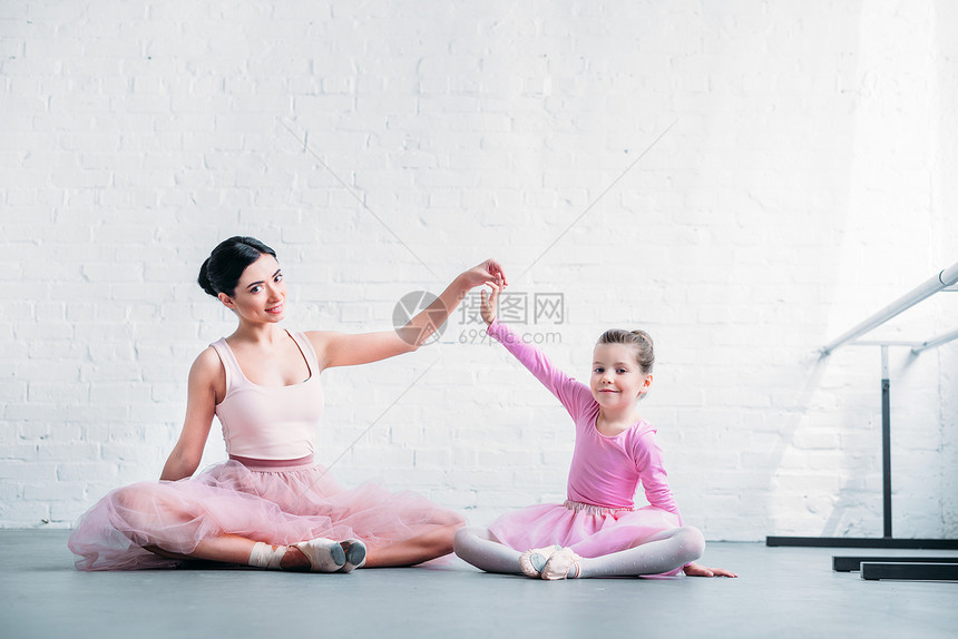 穿着粉色芭蕾舞短裙的漂亮成人和小芭蕾舞演员坐在芭蕾舞工作室图片