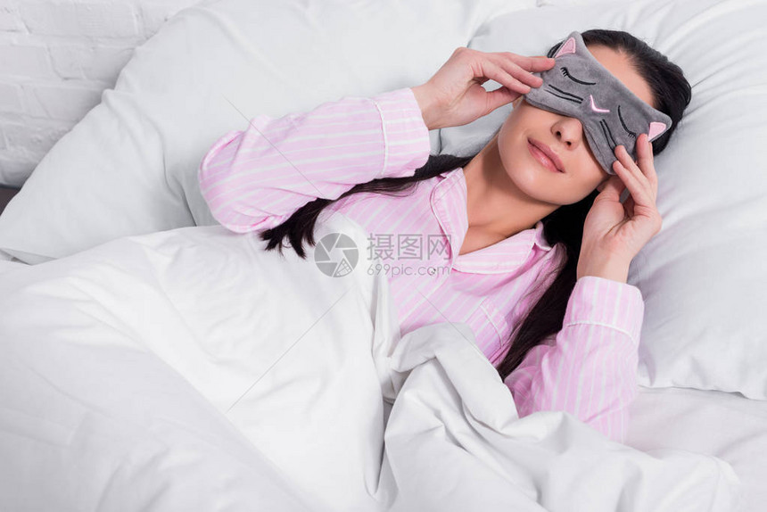穿着粉色睡衣和睡着面具的妇女躺图片