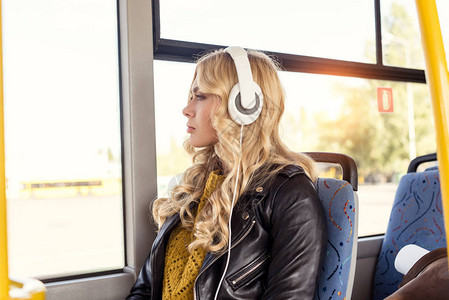 年轻体贴的女在乘坐公共交通工具时戴着耳机听图片