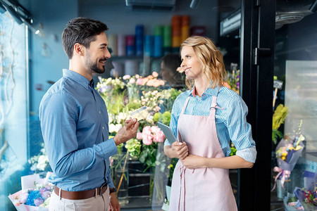 带信用卡的男客户和带数字平板电脑的花店在花店互相图片