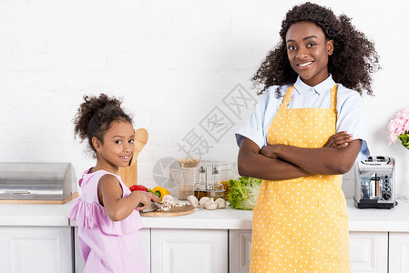 非洲裔美国母亲带着横跨双臂女儿在厨房图片