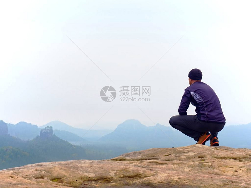 身穿黑裤子外套和黑帽子的成人游客坐在悬崖边缘上图片