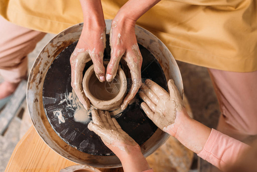 老师和孩子在陶轮上制作陶瓷锅的俯视图图片