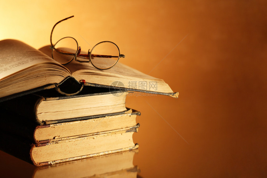 古老的书和眼镜堆放在精美的梯度背景上图片