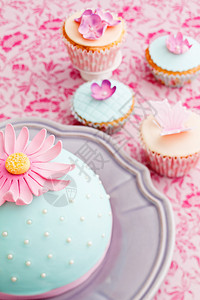 用粉红色糖花和糖蝴蝶装饰的圆形蛋糕和纸杯蛋糕图片