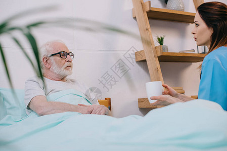 护士给躺在床上的老年病人送杯子和饮料图片