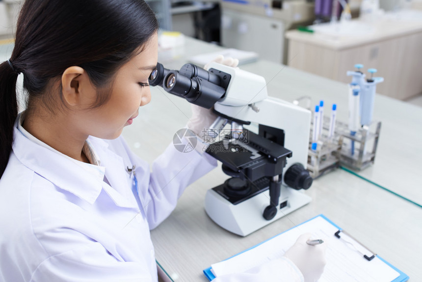 在实验室使用显微镜的年轻女科学研究员图片