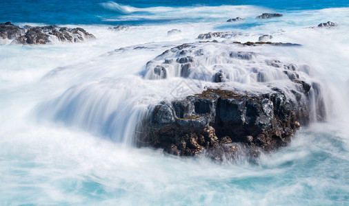 海浪在夏威夷KauaiQueensBath附近海岸边缘熔岩石上流背景图片