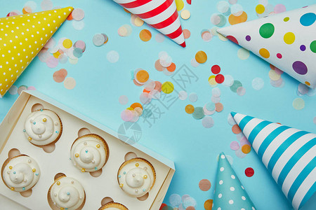蓝色背景上的美味纸杯蛋糕派对帽和彩色纸屑的顶视图图片