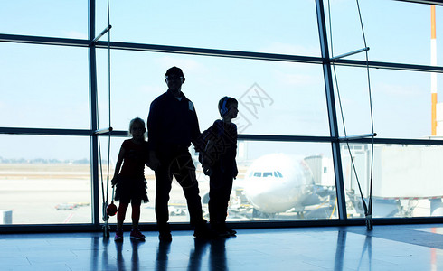 父亲和两个孩子站在机场窗前的剪影图片