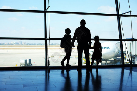 父亲和两个孩子站在机场窗前的剪影图片