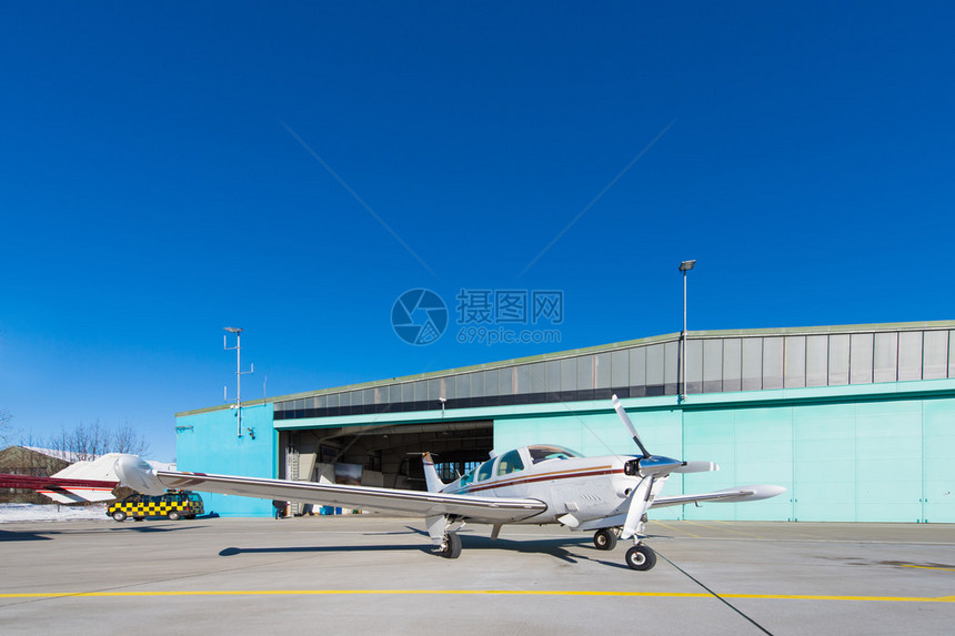 小飞机站在蓝天的飞机库前图片