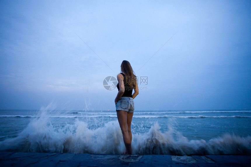 站在后面看着海浪拍打岸边的女人图片