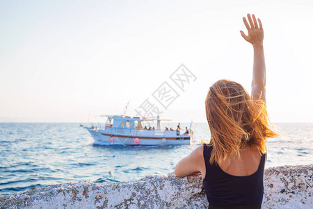 年轻女子从码头向小船挥手致意图片